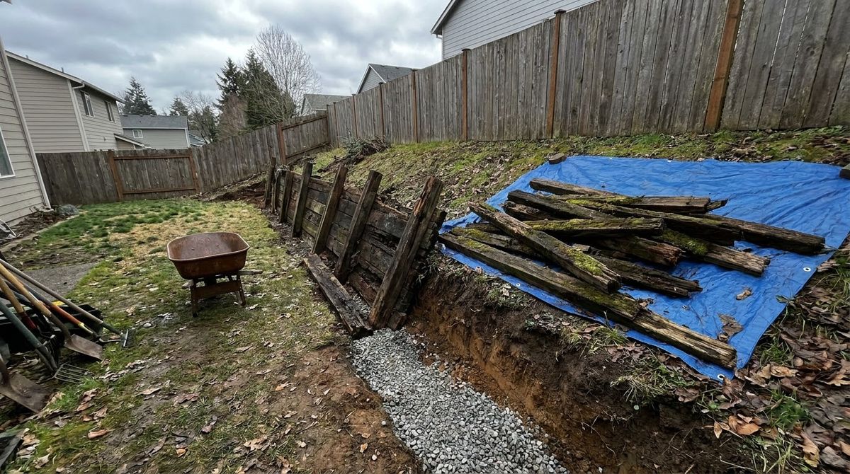 Leaning rotted timber retaining wall half removed, old timbers stacked for hauling away