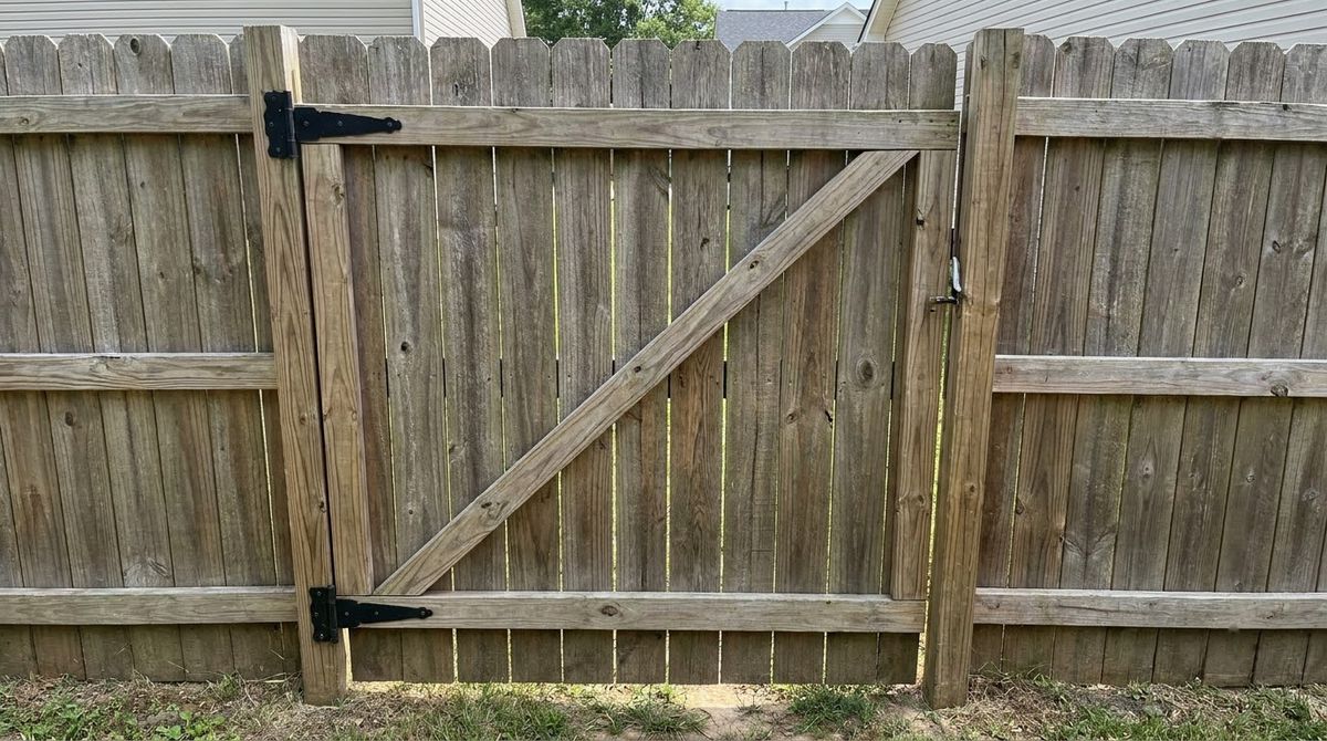 Wood privacy fence gate with a diagonal brace and black hinges hung between two posts