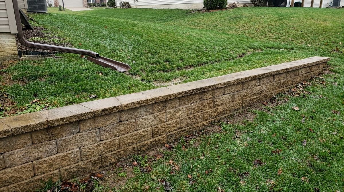 Shallow grassy swale running along the top of a capped segmental block retaining wall