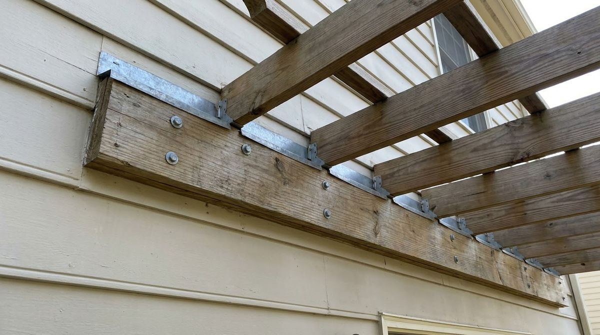 Pergola ledger board lag-bolted to a house wall with metal flashing above it