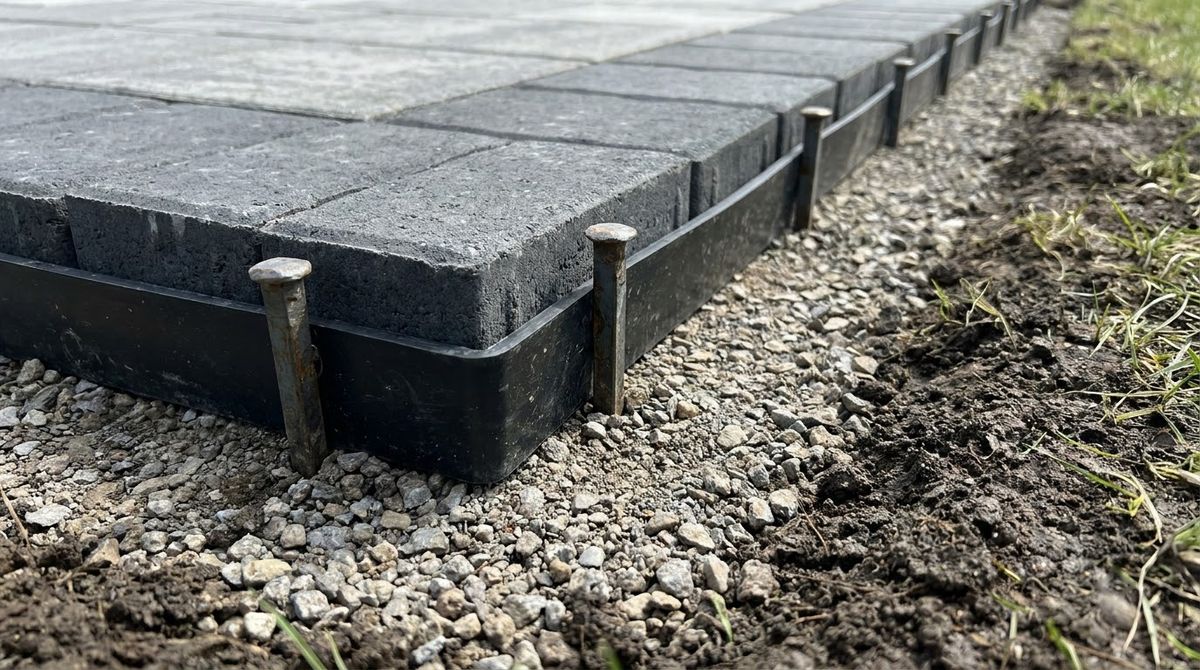 Black plastic paver edge restraint spiked into gravel base along a new patio edge