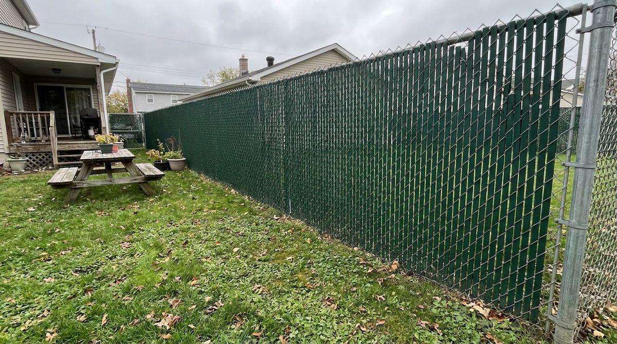 Galvanized chain-link fence with green privacy slats woven into the mesh along a backyard