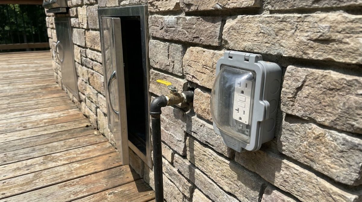 Gas shutoff valve and weatherproof GFCI outlet with in-use cover beside a deck kitchen