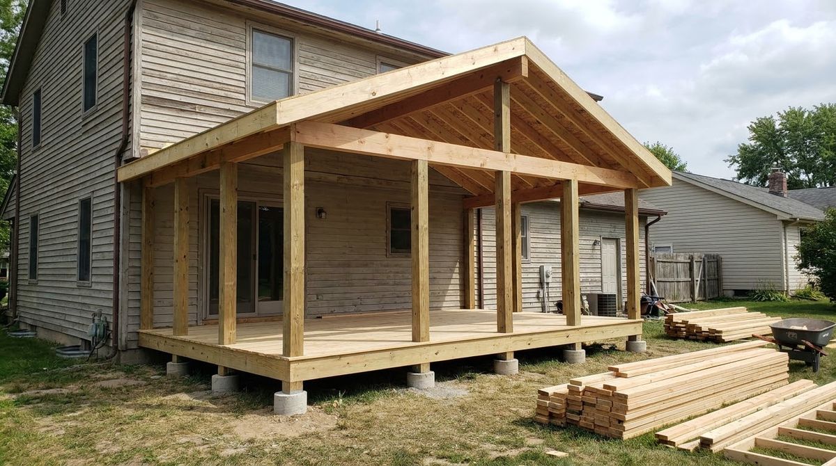 Gable roof rafters and posts framed over a porch deck before screens and shingles