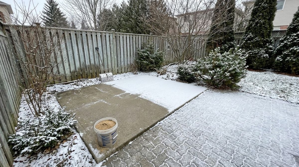 Snow-dusted concrete patio and paver patio in a cold US backyard in winter