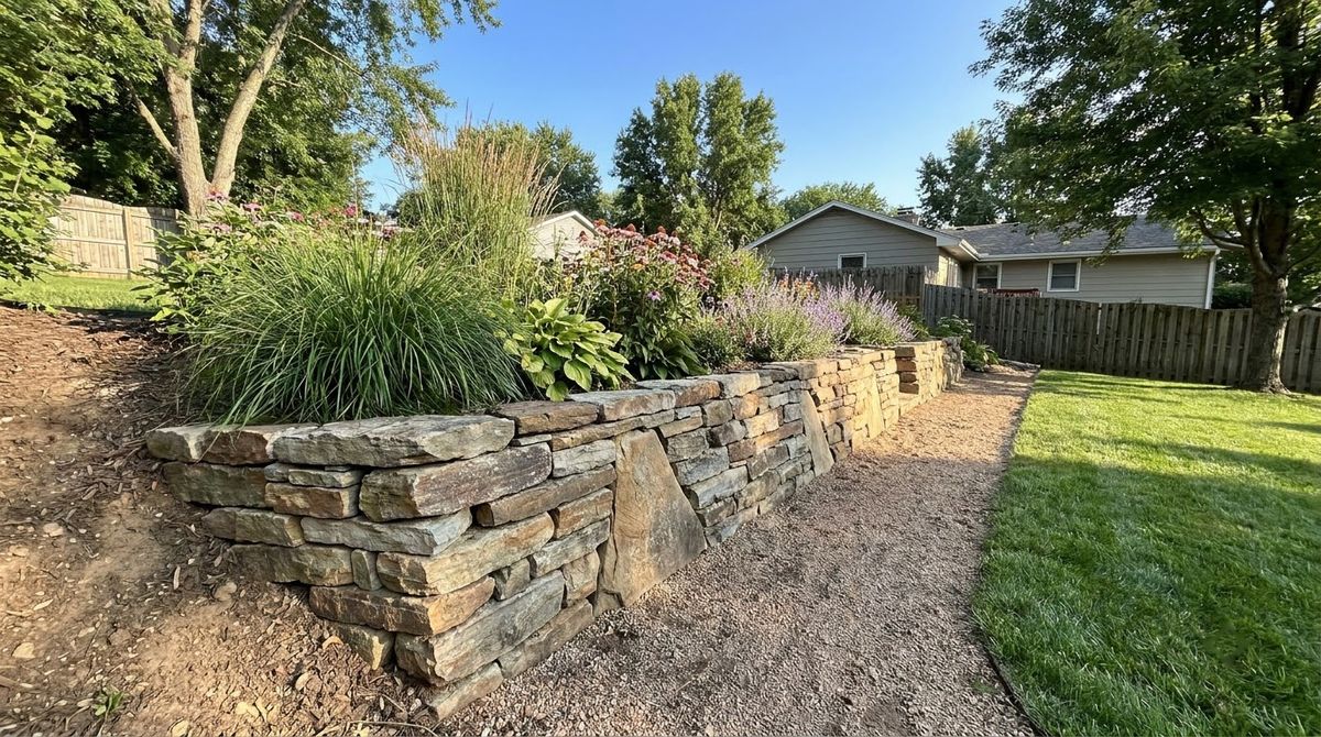 Low dry-stacked natural stone retaining wall leaning into a garden bank with perennials