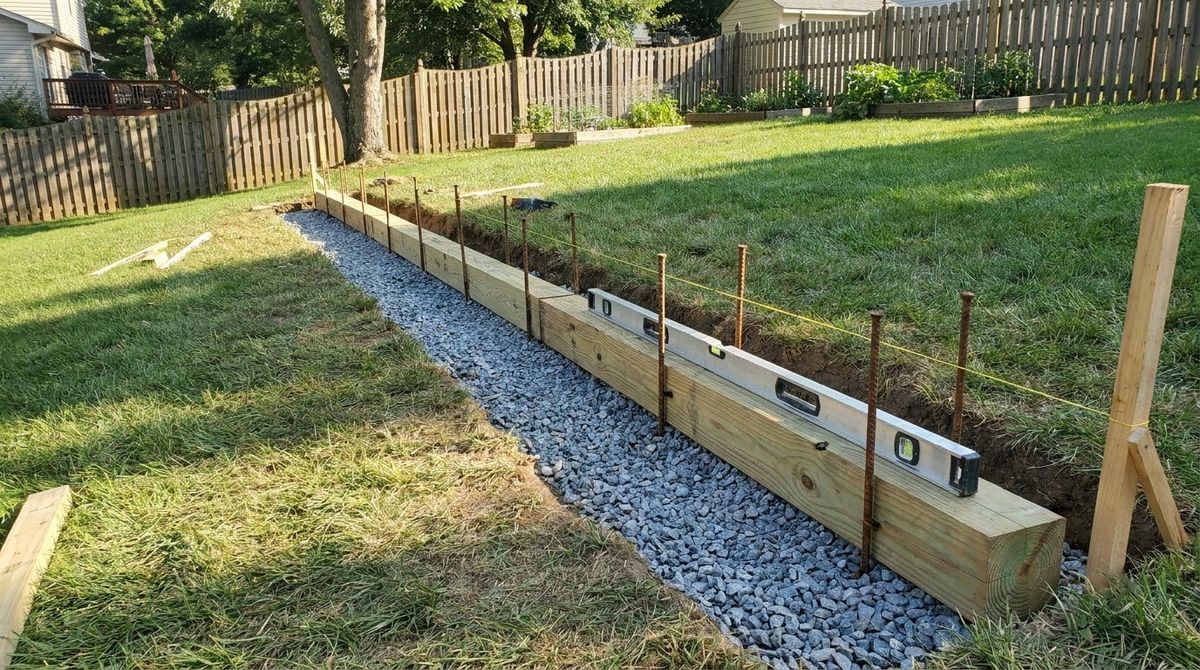 First course of treated timbers set level on crushed stone in a shallow trench with rebar pins