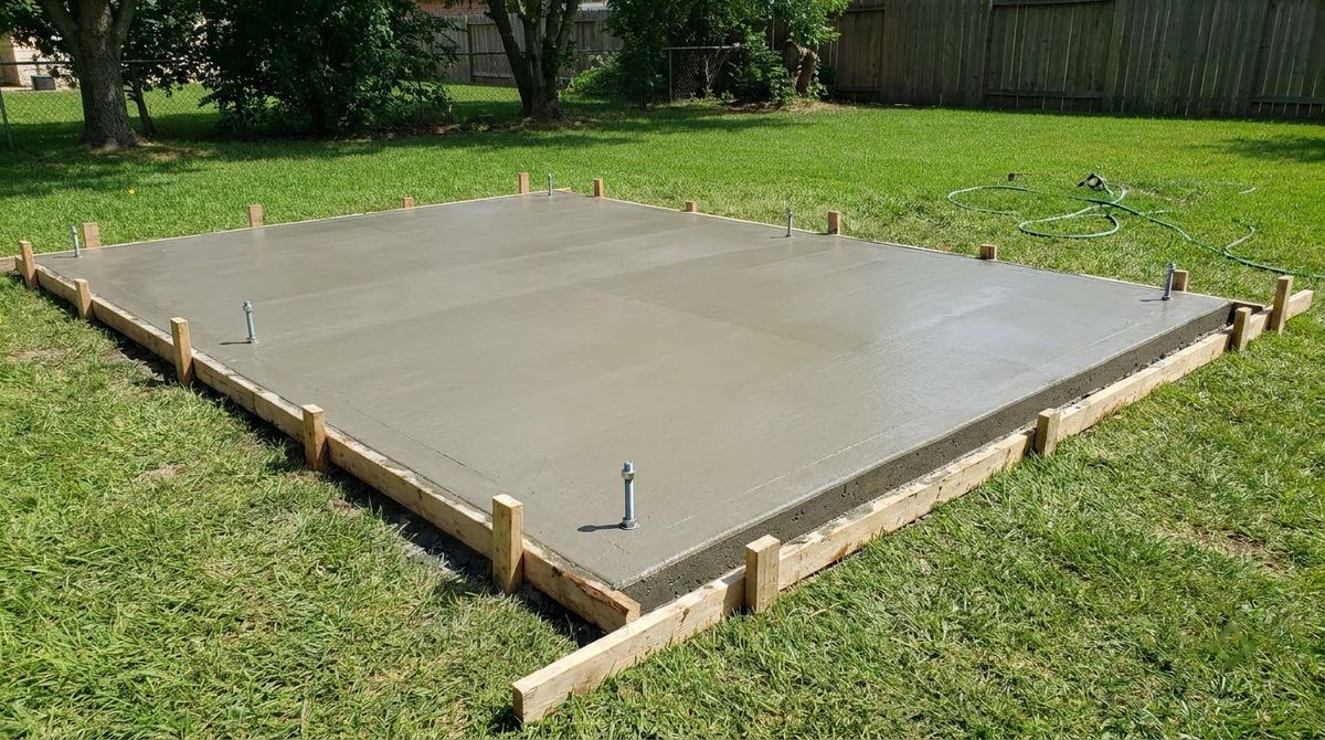 Fresh concrete shed slab with anchor bolts along the edge, raised above the yard