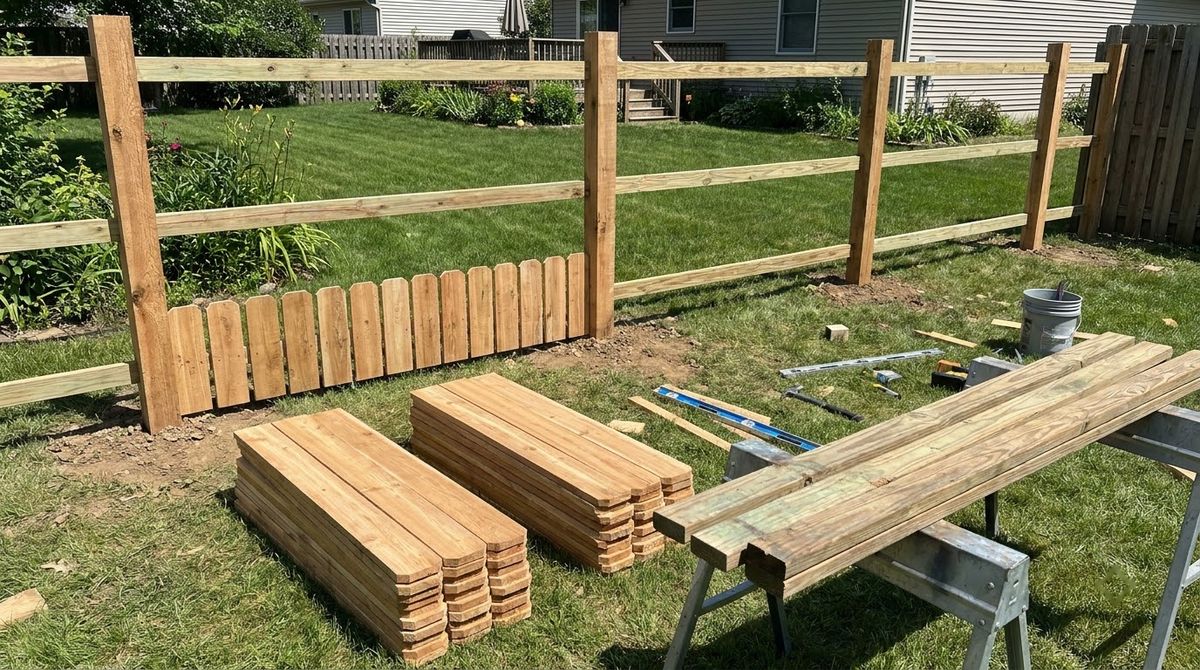 Stacks of cedar fence pickets and treated rails beside a partly built wood fence bay