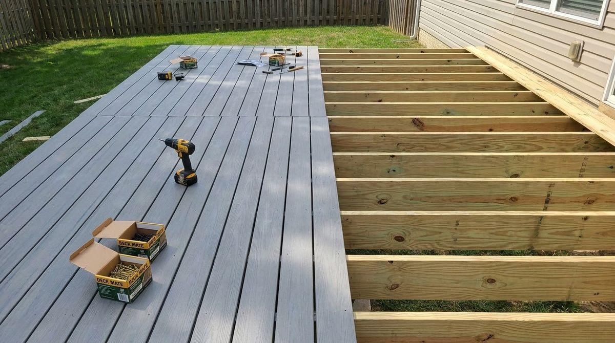 Gray composite deck boards being laid on a pressure-treated wood joist frame in a backyard