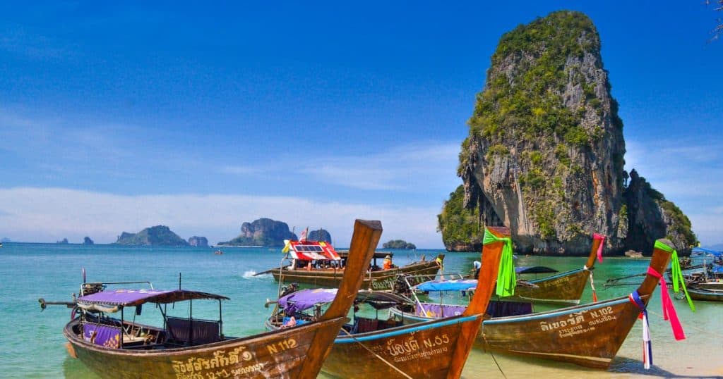 Traditional longtail boats anchored on the beach at Railay with limestone cliffs in the background.