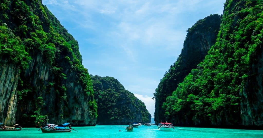 Scenic tropical lagoon surrounded by lush green limestone cliffs with boats on clear turquoise water.
