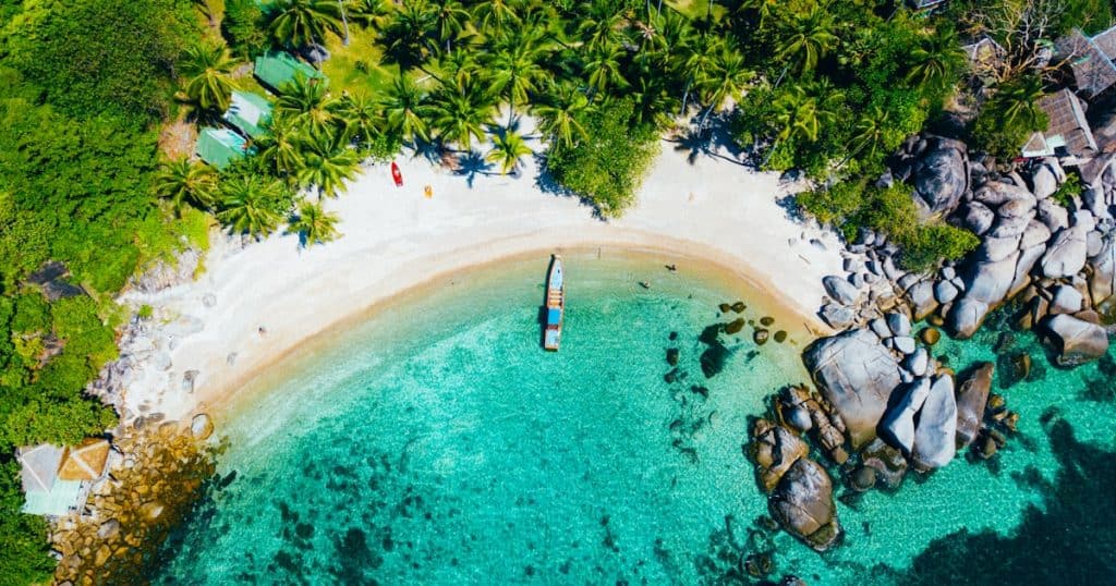 Beach with turquoise water and white sand, surrounded by lush greenery and rocks.
