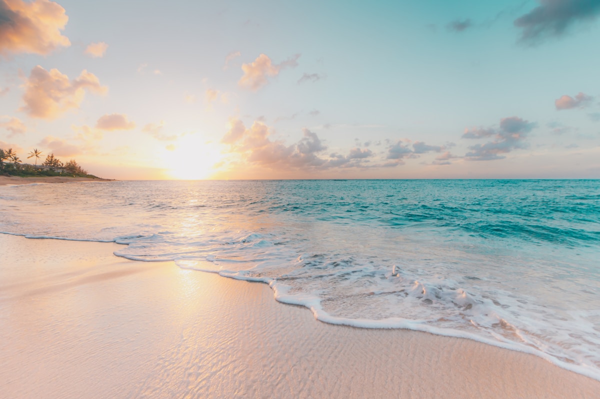 Lone person walking along an empty stretch of Phuket beaches at sunrise with gentle waves