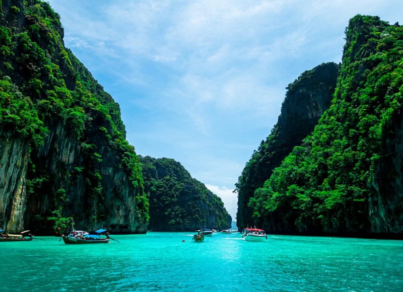 Crystal clear turquoise water with traditional Thai longtail boats at a white sand beach in Phuket Thailand