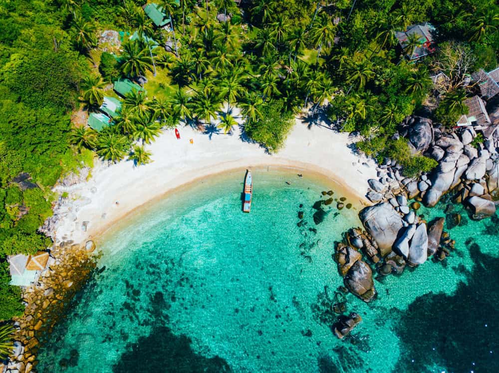 Crystal clear turquoise water at a tropical island with white sand beach surrounded by lush green vegetation in Thailand