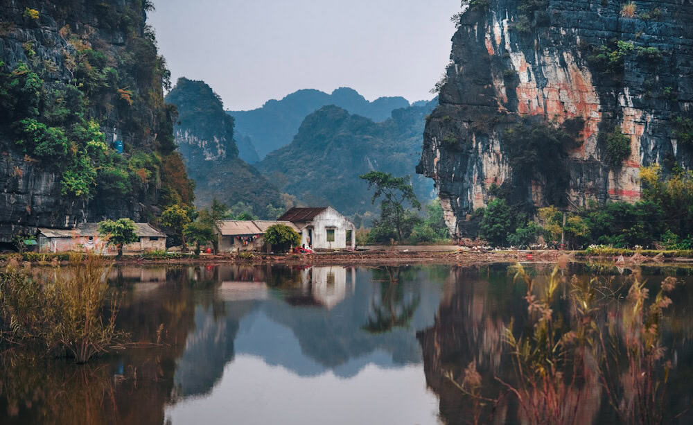 Group of tourists on a colorful longtail boat cruising through clear turquoise water past dramatic limestone karst cliffs in Thailand