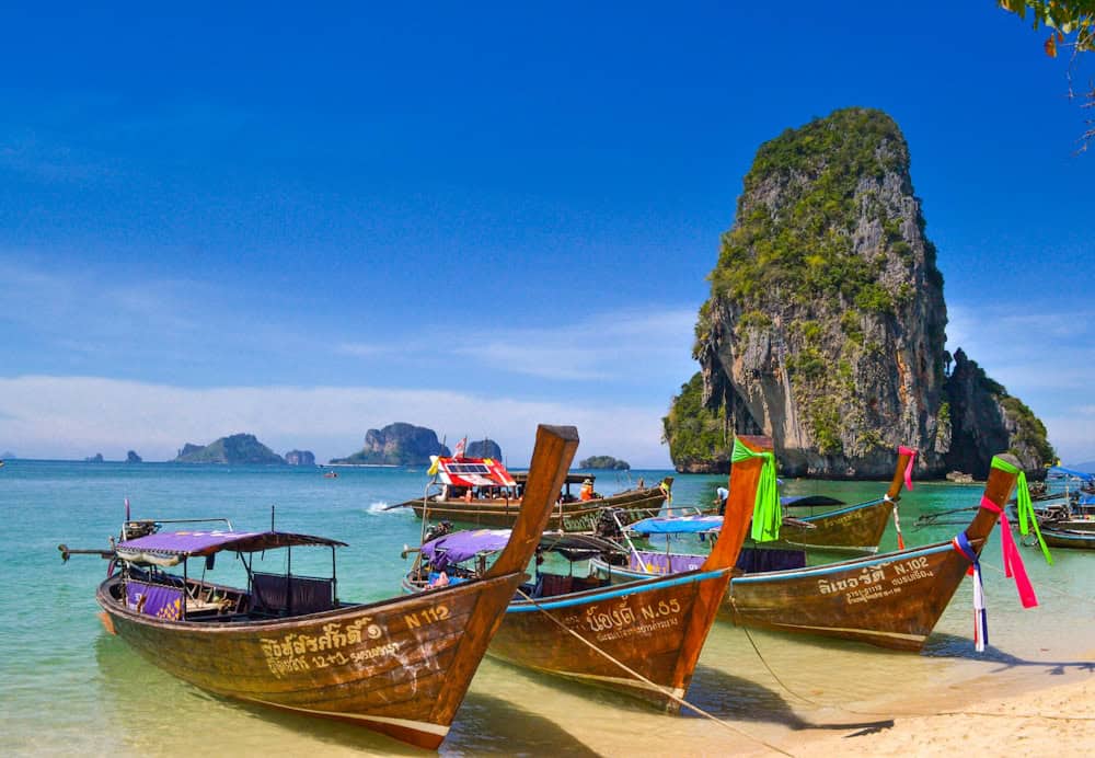 Calm turquoise waters and white sand at Kata Beach Phuket with longtail boats anchored near shore and palm trees framing the tropical bay scenery