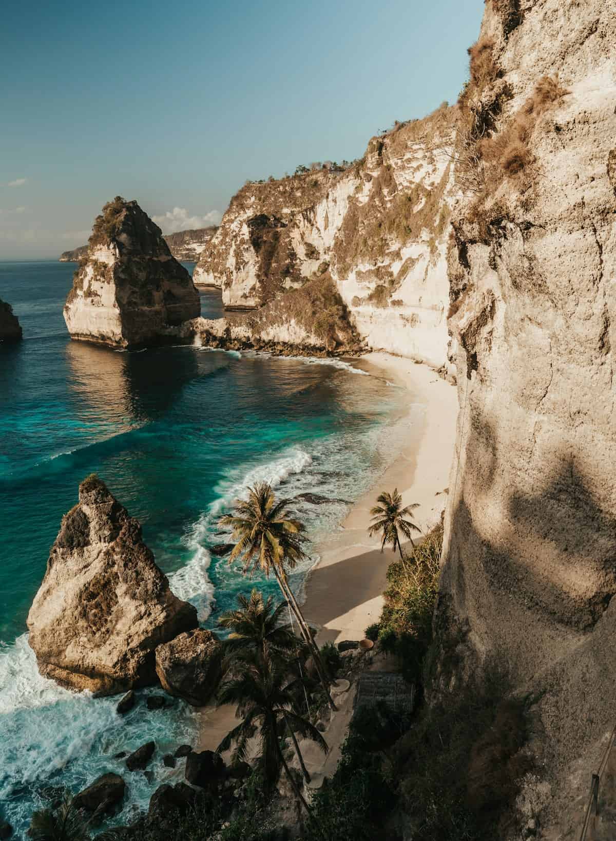 Aerial view of a stunning turquoise infinity pool overlooking Bali jungle with palm trees and rice terraces in the golden hour light