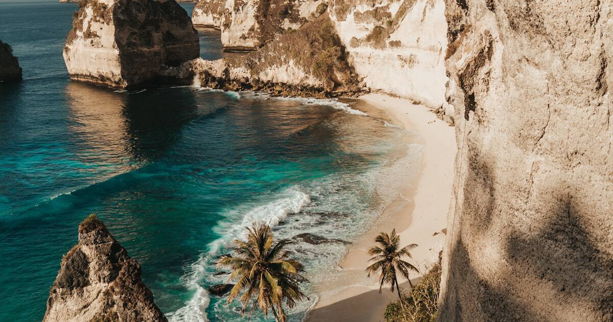 Aerial view of a stunning turquoise infinity pool overlooking Bali jungle with palm trees at golden hour