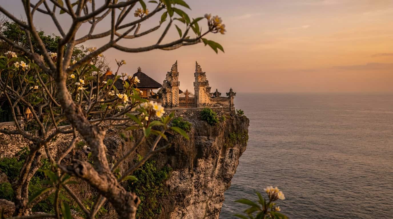 Uluwatu Temple in Bali on a limestone cliff overlooking the Indian Ocean with frangipani tree in foreground and warm afternoon light