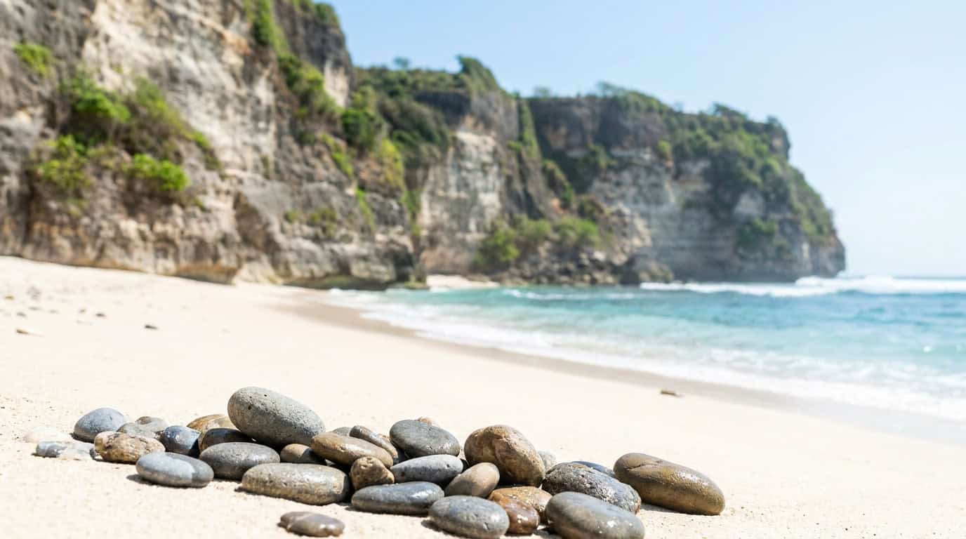 Deserted stretch of white sand Melasti Beach in Bali with towering limestone cliffs gentle turquoise waves and beach pebbles in foreground