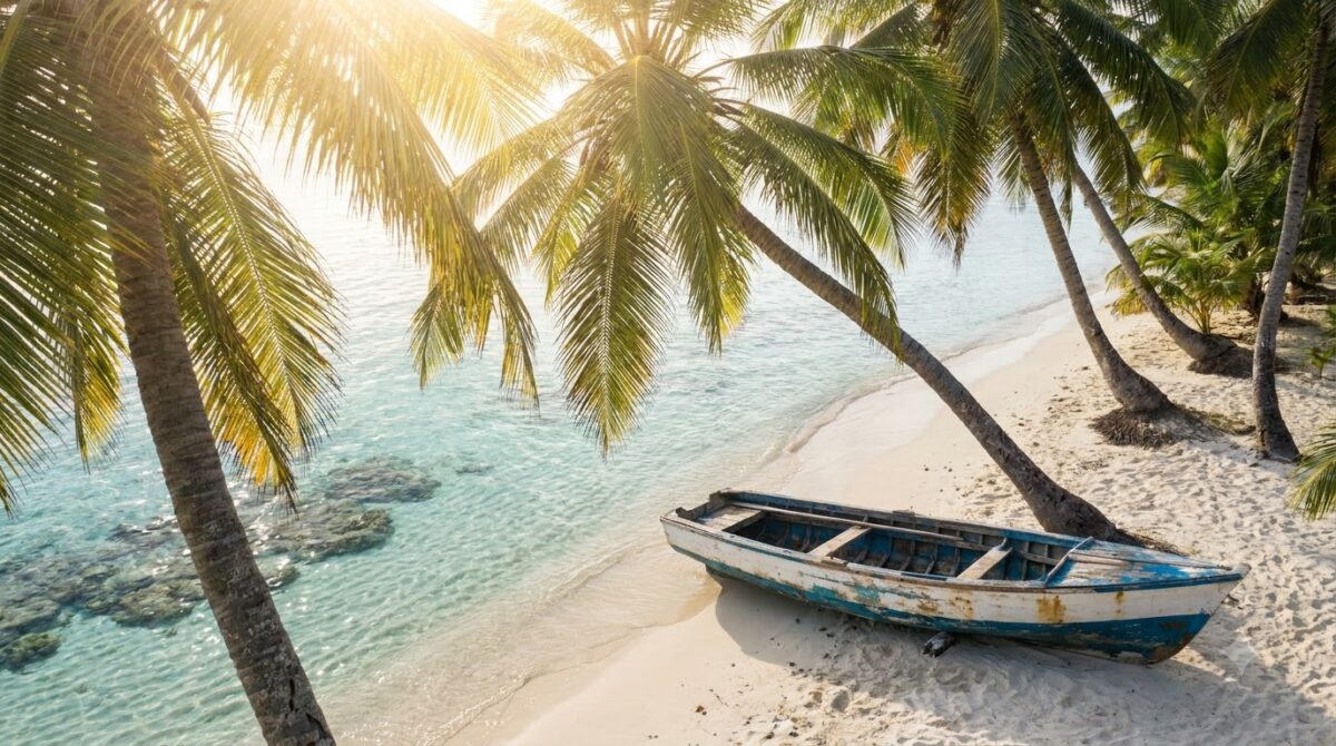 White sand Caribbean beach with leaning palms and a wooden boat on the shore