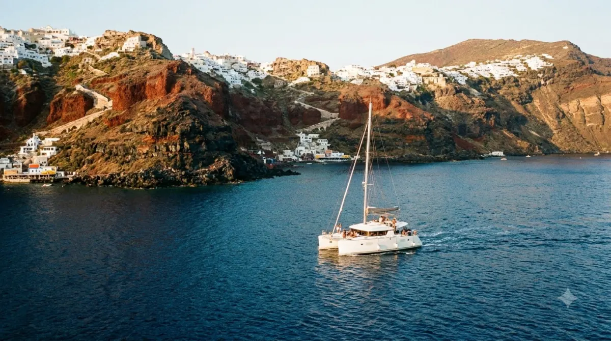 A catamaran on blue water below the volcanic cliffs of the Santorini caldera