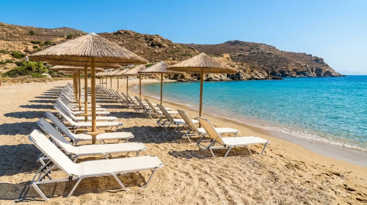White sun loungers and umbrellas on a sandy beach with turquoise water in Mykonos