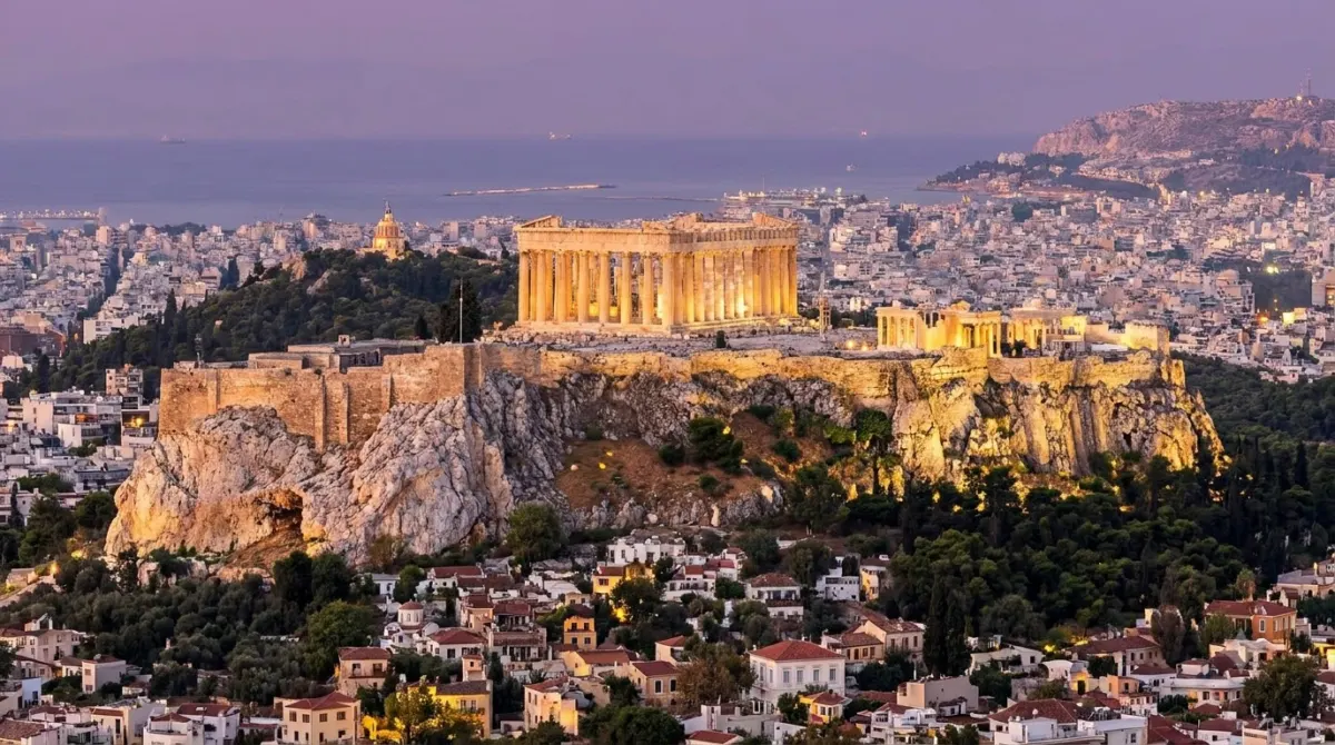 An ancient temple on a rocky hill above a city at dusk in Greece