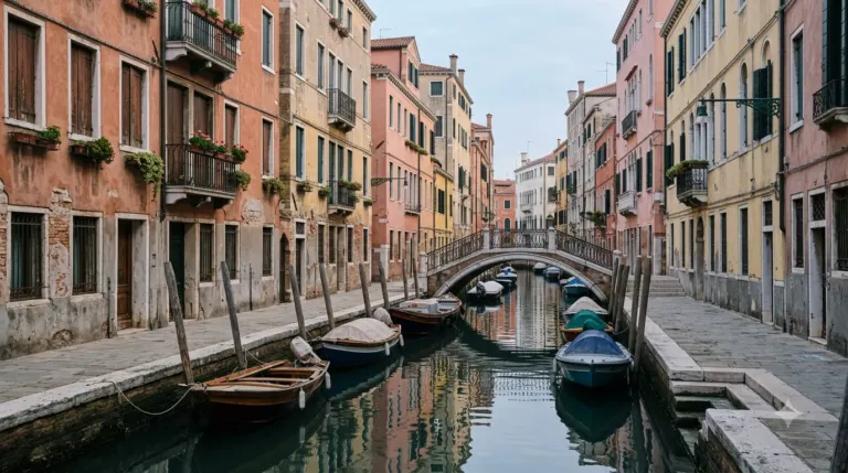 A narrow Venetian side canal with pastel buildings and a small bridge in early morning