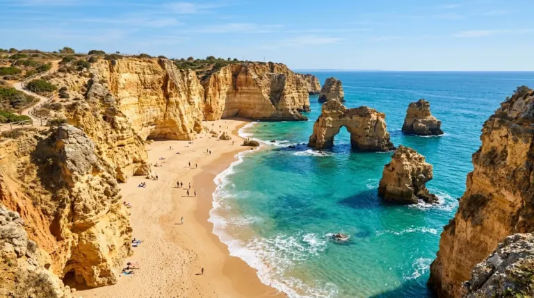 Golden sandstone cliffs and sea stacks above a small sandy cove with clear water in the Algarve