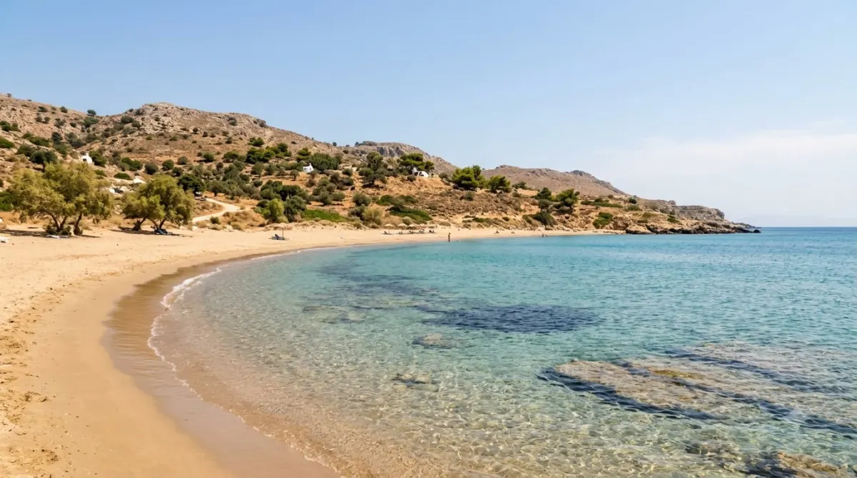 A calm sandy beach with clear turquoise water and low hills behind on the east coast of Rhodes
