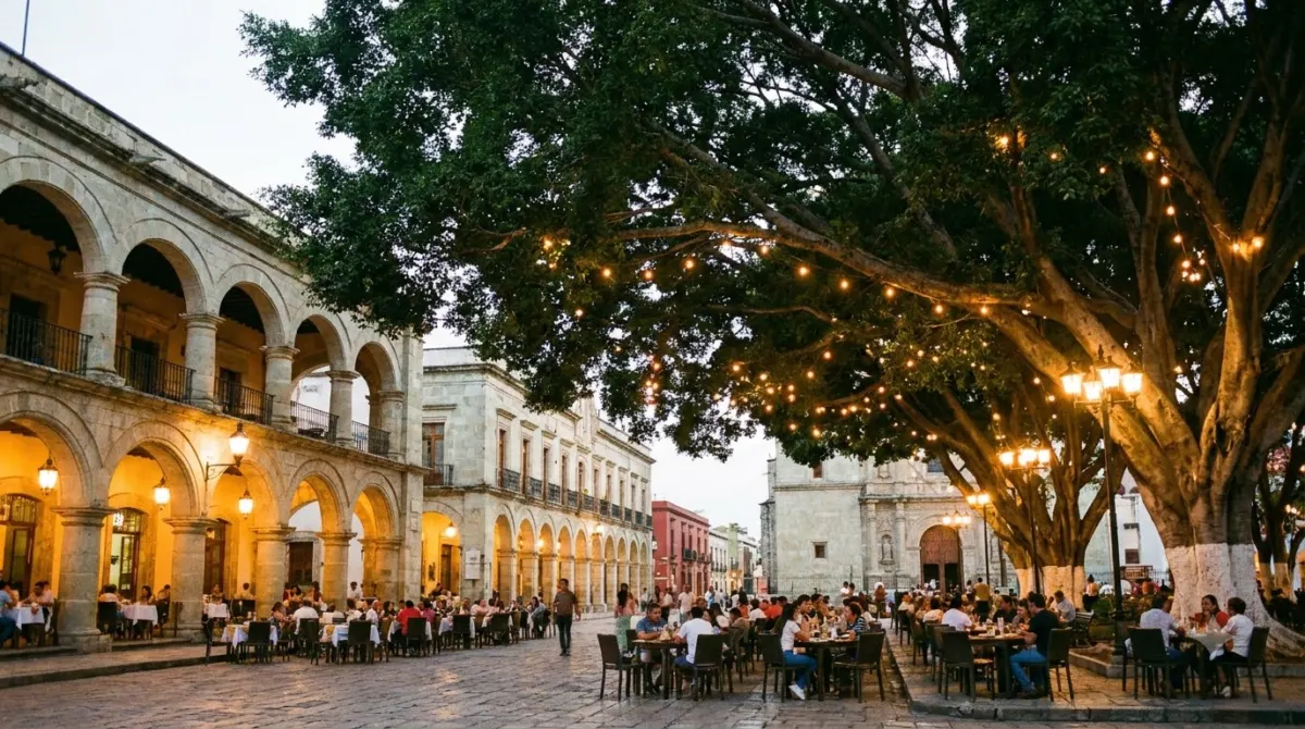 A tree filled colonial main square with arcades and cafe tables at dusk, Oaxaca City, Mexico