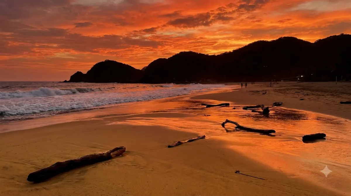 A long open beach at sunset with dark hills at one end and orange sky, Zipolite, Oaxaca, Mexico
