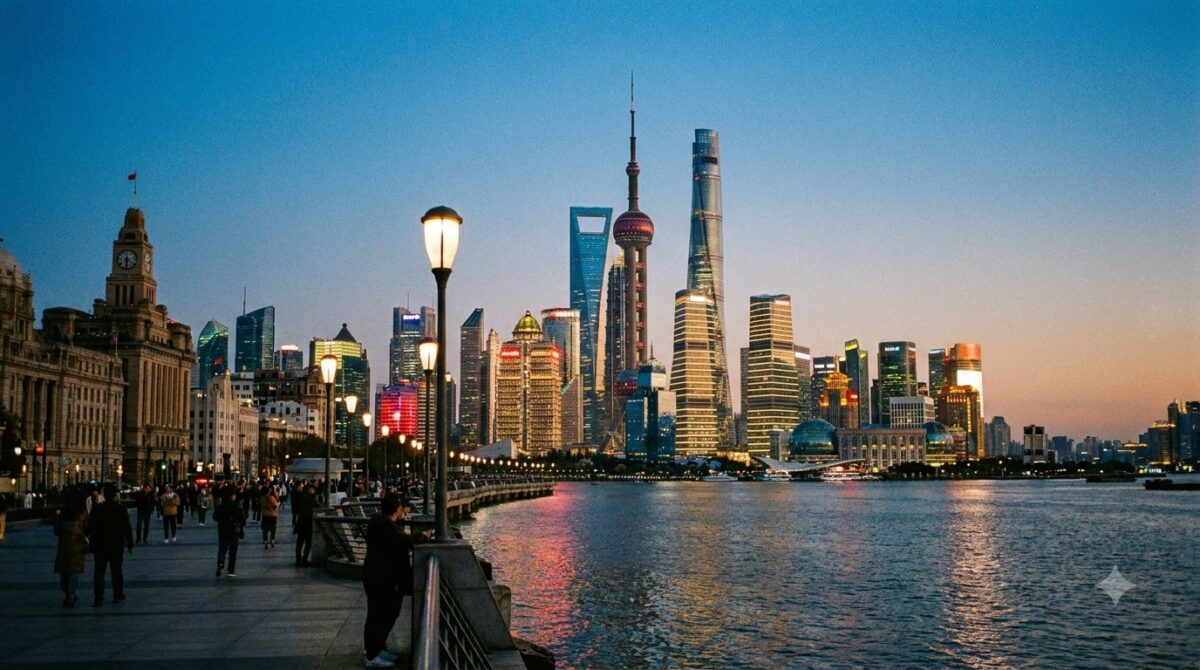 The Shanghai skyline of glass towers across a river at dusk with a stone waterfront promenade