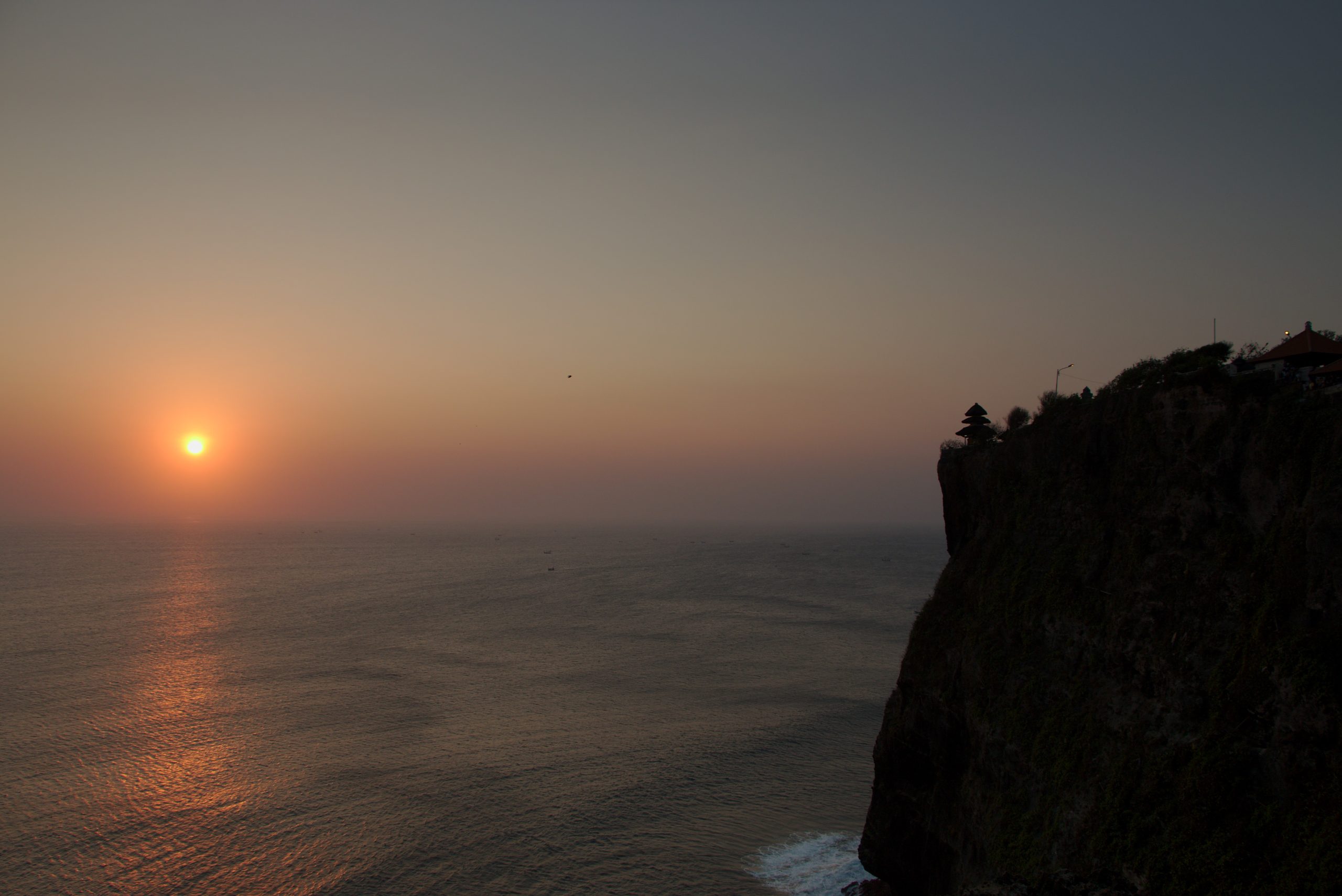 Golden sunset silhouette of Uluwatu cliff temple perched above the Indian Ocean in Bali