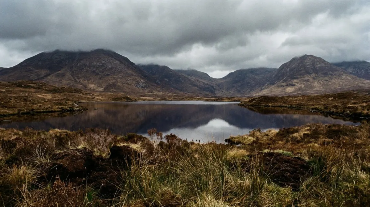 A still lake reflecting bare mountains under a grey sky, Connemara, County Galway, Ireland