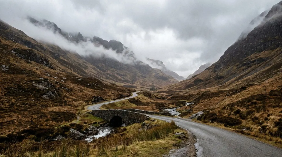 A single track road running through a steep mountain glen with heather and low cloud, Scottish Highlands