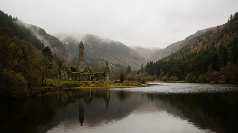 A stone round tower and ruined church beside a lake in a wooded glacial valley, Glendalough, County Wicklow, Ireland