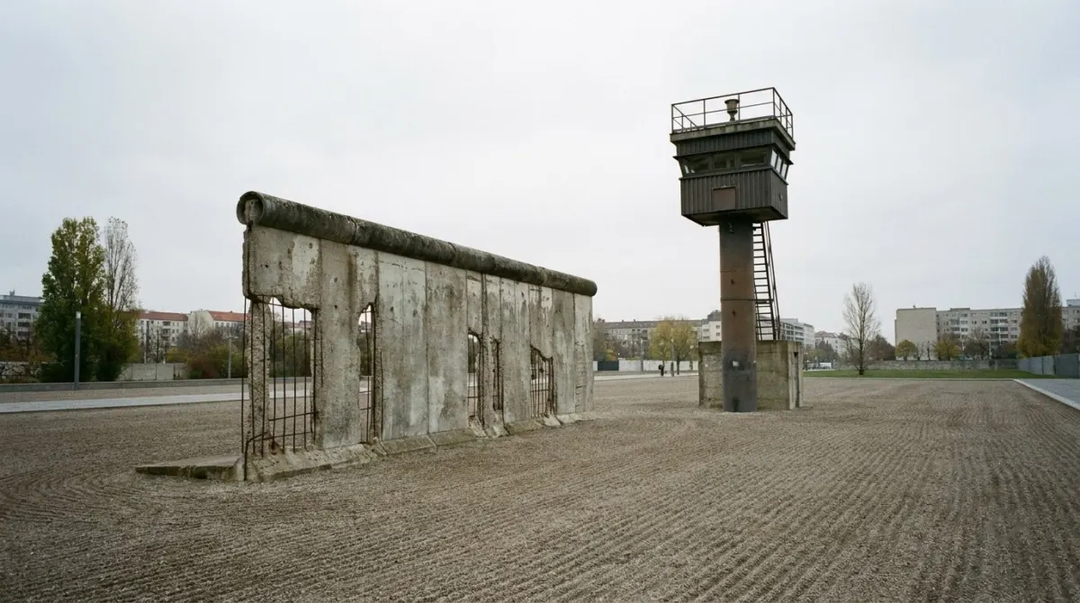 A preserved section of concrete wall with a watchtower and open ground behind it, Berlin Wall Memorial, Germany