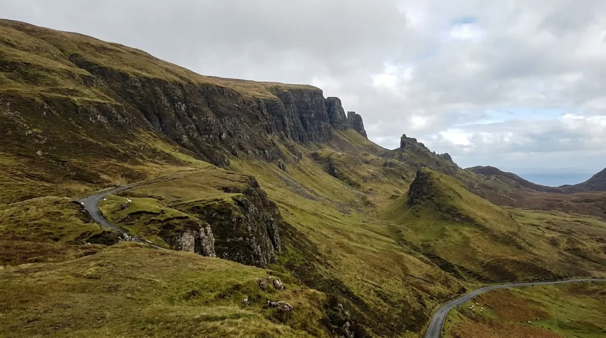 A single track road winding below jagged green rock formations on a hillside, the Quiraing, Isle of Skye