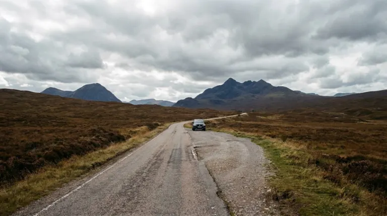 A single track road with a passing place sign winding across open moorland towards mountains, Scottish Highlands