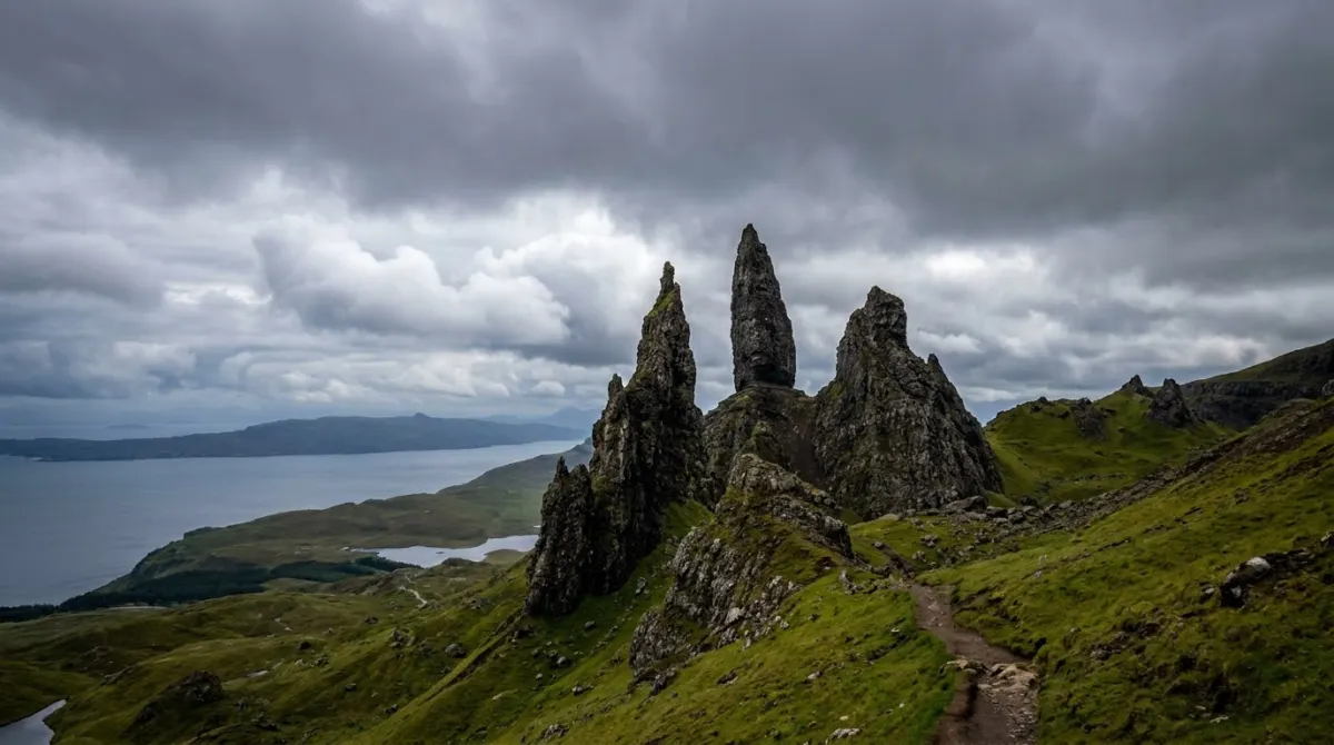 A tall rock pinnacle rising from a green ridge above a sea loch, the Old Man of Storr, Isle of Skye