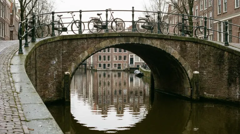 A canal bridge with bicycles and narrow gabled houses reflected in the water, Amsterdam, Netherlands