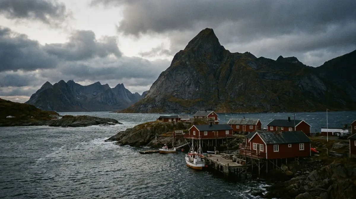 Jagged mountains rising straight out of the sea above a fishing village with red wooden huts, Lofoten, Norway