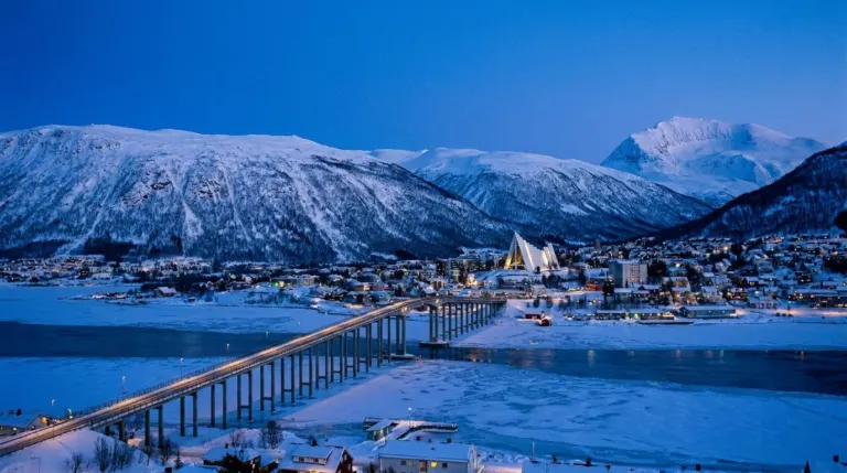 A small Arctic city on an island with snow covered mountains behind and a bridge across the sound, Tromso, Norway