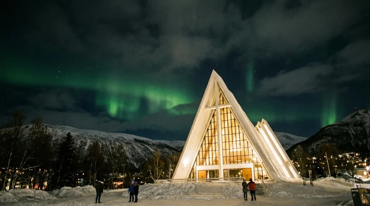 A white triangular modern cathedral lit at night under a green aurora sky, Tromsdalen, Norway