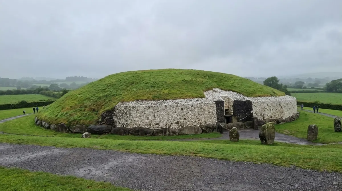 A large round grass-topped passage tomb ringed with white quartz stones under a grey sky, Newgrange, Boyne Valley, Ireland