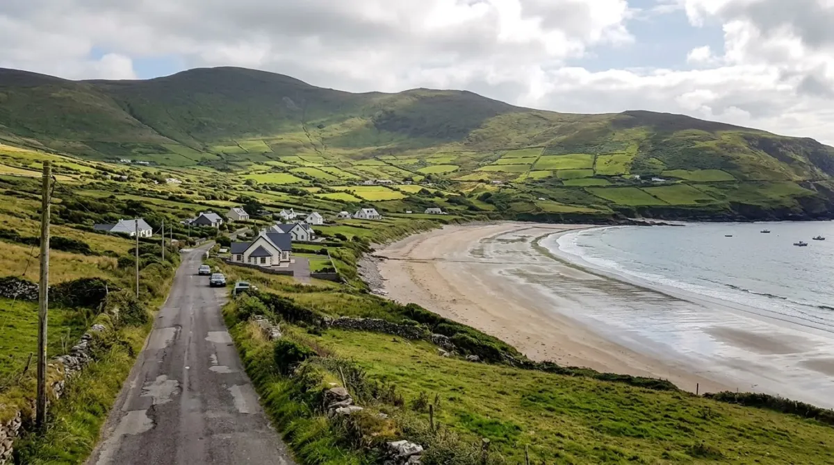 A road beside a wide sandy bay with a few guesthouses and green hills behind, Ventry, Dingle Peninsula, Ireland
